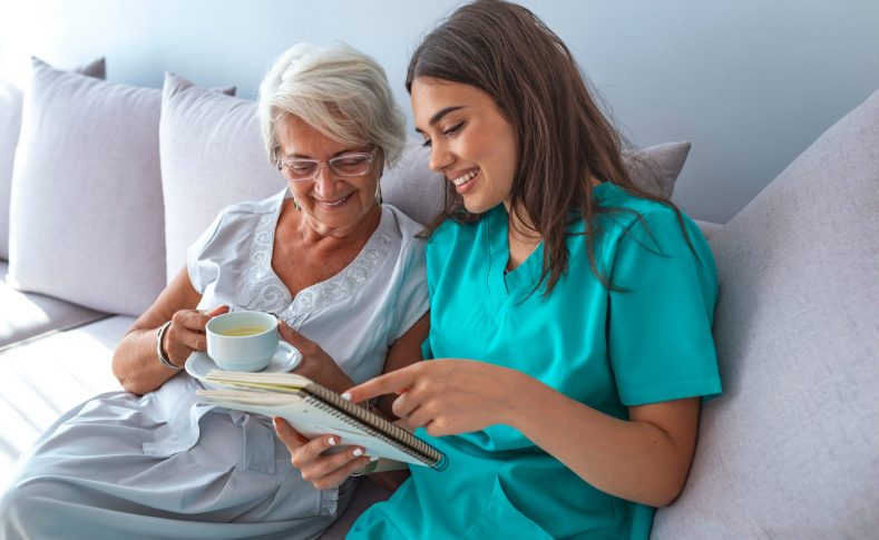 Happy patient is holding caregiver for a hand while spending time together. Professional helpful caregiver comforting smiling senior woman at nursing home